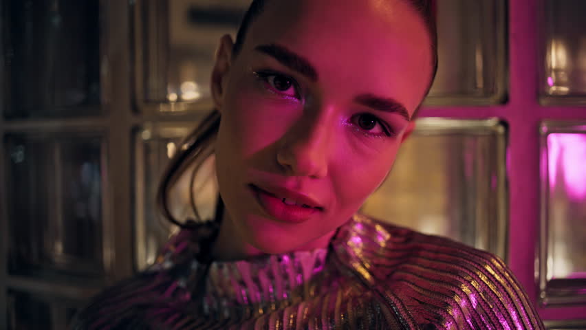 Portrait of bright attractive party girl looking camera in front glass wall. Beautiful sexy woman with shiny makeup posing alone at night close up. Confident gorgeous model wearing sparkling clothes