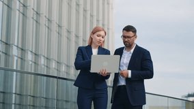 Gimbal shot two business partners caucasian man woman in formal suits standing outdoors office building terrace discussing upcoming project and deals using laptop. Corporate employees in downtown city - Powered by Shutterstock - Get 15% off with code: PIKWIZARD15