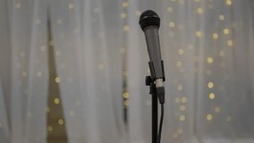 Wedding Day stock clip of mic microphone on stand with led bokeh lights in background and white backdrop ready for performer singer artist or toast speeches. Slow and slight push in shot.