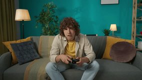 Young man in casual clothing, sitting on the sofa in the living room playing video game