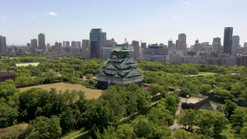 Aerial rising over historic Osaka Castle with park, moat, skyscraper, and city in Osaka, Japan. Royalty-Free Stock Footage #1107189343
