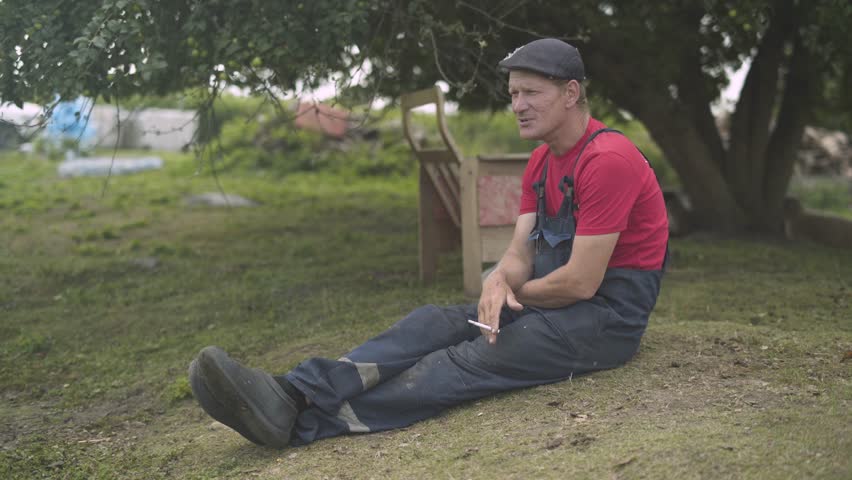 Farmer sitting on the grass smoking cigarette.
