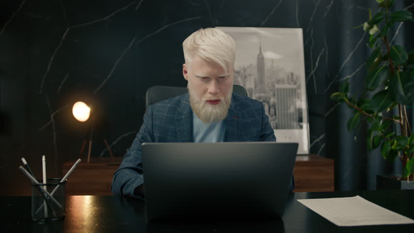 Thoughtful serious young white hared albino businessman sitting at office desk with laptop thinking of inspiration, calculating cost, search problem solution ideas, lost in thoughts concept dreaming Royalty-Free Stock Footage #1107193441