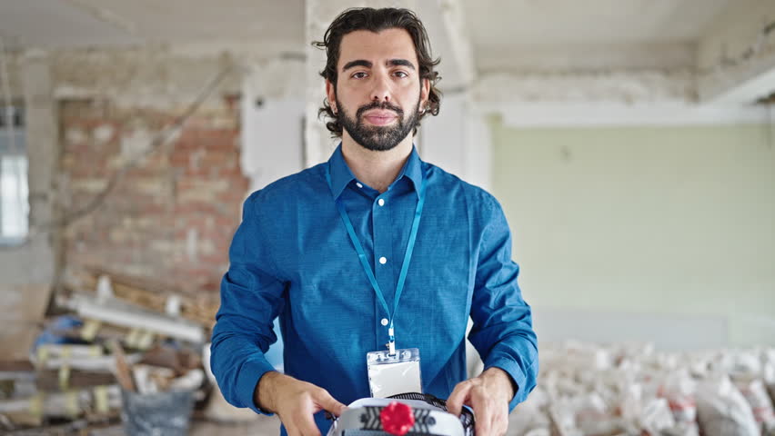 Young hispanic man architect wearing hardhat smiling at construction site