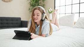Young blonde woman watching video on touchpad lying on bed at bedroom