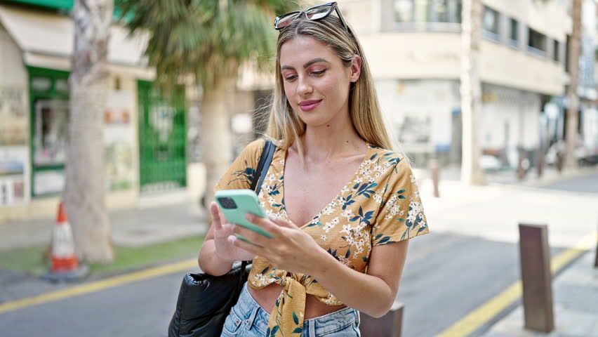 Young blonde woman using smartphone with winner expression at street