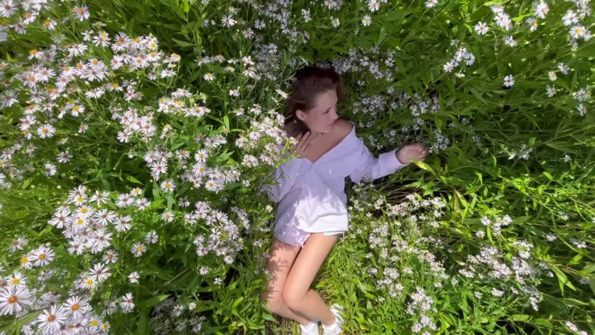 beautiful young woman lies in flowers of daisies in a field top view. The concept of the joy of life and outdoor recreation of a girl.