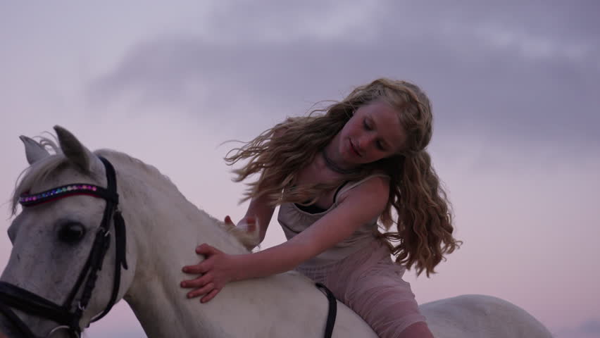 A girl gently strokes the silky coat of a white horse showing its love and affection for the animal