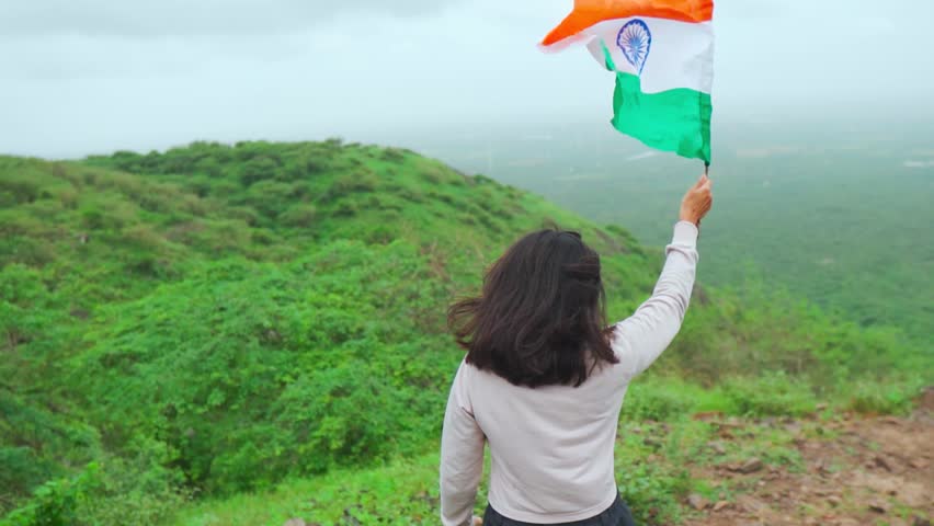 Indian girl waving Indian flag while standing on top of the mountain at Nanamo Hill, Kutch, India. People celebrating republic day outdoors. Female waving flag on mountain summit. 