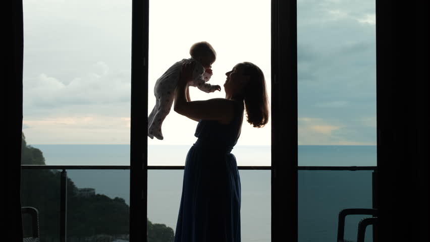 Young woman playing with her cute baby on the balcony of hotel room, slow motion. Mother lifting her infant daughter over head Royalty-Free Stock Footage #1107216401