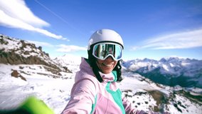 Smiling woman blogger vlogger standing on top mountain talking with camera recording video. Female skyer in protective clothing helmet goggles. Create content for blog, vlog. Winter sport resort.