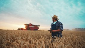 Farmer agronomist man manager in straw hat with tablet works walks on field controls combine harvester harvesting ripe wheat. Food production, farm, farmland, farming industry, agribusiness concept. - Powered by Shutterstock - Get 15% off with code: PIKWIZARD15