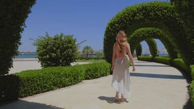 Woman is walking on a path with green arcs. Girl with beautiful long hair. Slow motion video. Sea and palms on the background. 