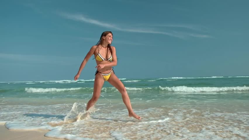 Beautiful young woman in yellow bikini jumping on the beach at sunny day in summer. Side view of beautiful female jumping at beach on a sunny day Tropical landscape. Sexy back of slim girl, clear