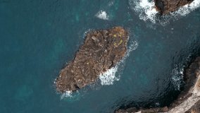 small rocky island with stone texture in open blue sea, aerial view 4k