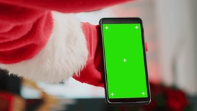 Vertical video Staff assistant wearing Santa Claus suit in shopping mall adorn with Christmas decorations holding chroma key phone, taking a break from work while watching videos on green screen - Powered by Shutterstock - Get 15% off with code: PIKWIZARD15