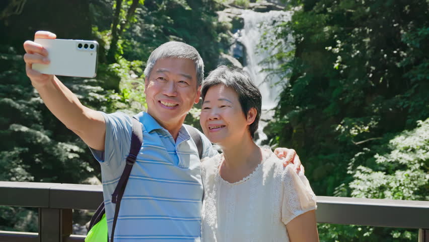 Old couple taking selfie in front of the waterfall and check the picture together | Shutterstock HD Video #1107234251