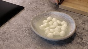 Balls of mozzarella cheese. A hand puts a plate of cheese on the table.