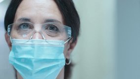 Senior female doctor in protective face mask and eyewear posing for camera in medical clinic. Close-up shot, video portrait