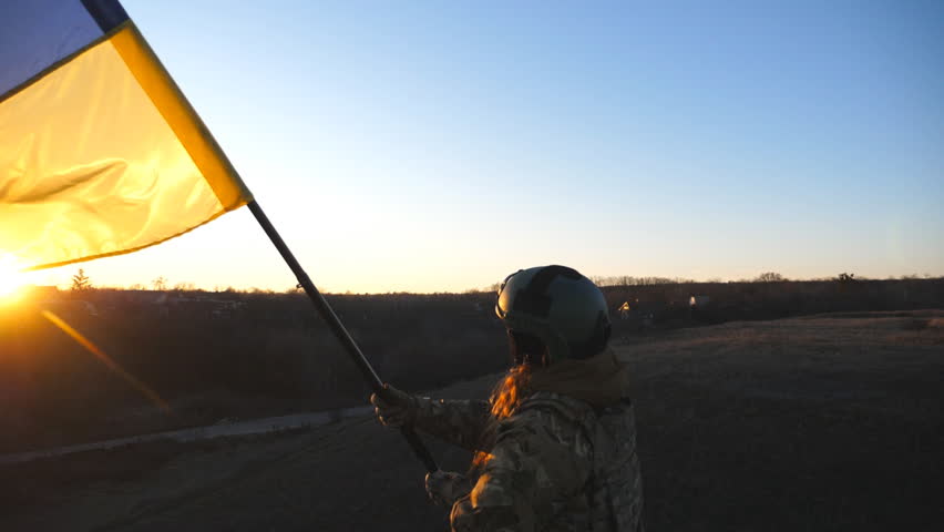 Dolly shot of young woman in military uniform waving blue-yellow flag against background of sunset. Female ukrainian army soldier lifting national banner in hill. Invasion of territory Ukraine concept Royalty-Free Stock Footage #1107242413