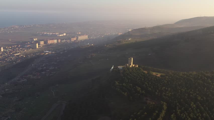A huge sign with the inscription "Derbent" on a mountain covered in evening mist. Dagestan, Russia.