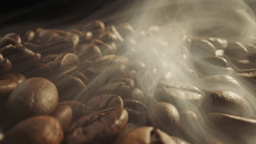Roasting coffee beans with smoke on dark background. Smoke comes from fresh coffee seeds. Slider shot of coffee beans during roasting. Super macro shot