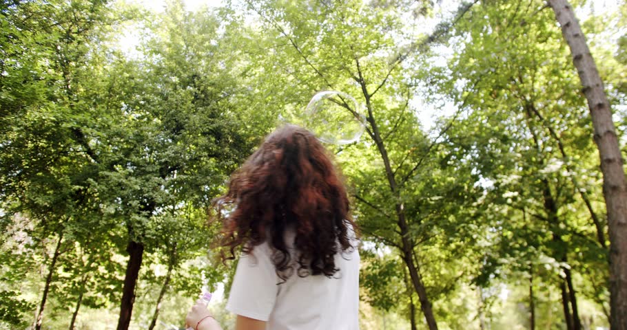 Young woman making large soap bubbles and smiling. Young One Woman Smiling Carefree Having Fun Blowing. Joy Girl Enjoying Holidays. fashionable young caucasian woman blowing soap bubbles in the nature