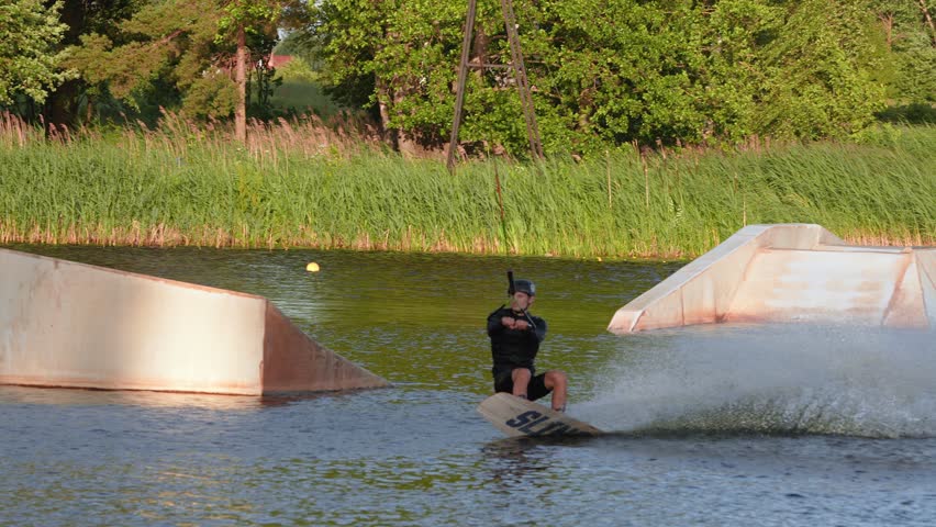 Young man wakeboarding in the park making difficult pro level wakeboard tricks. Extreme water sports. Action time in summer. Wakeboarder making tricks. 