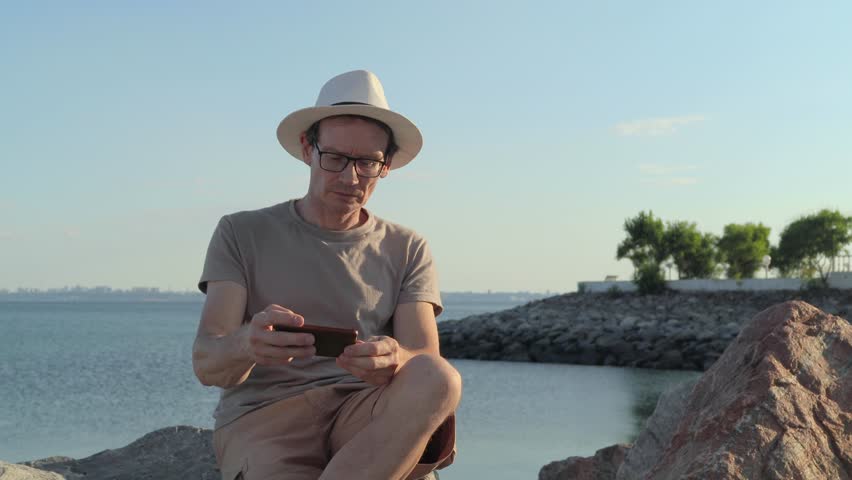 Middle Aged Man Using Phone By The Sea On Vacation
