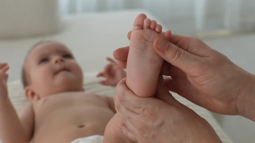 Closeup high-angle view of loving mother massaging newborn infant baby feet with thumbs tender touch parenting. Close up of young mom touching legs of little infant kid lying on bed at home. Royalty-Free Stock Footage #1107253943