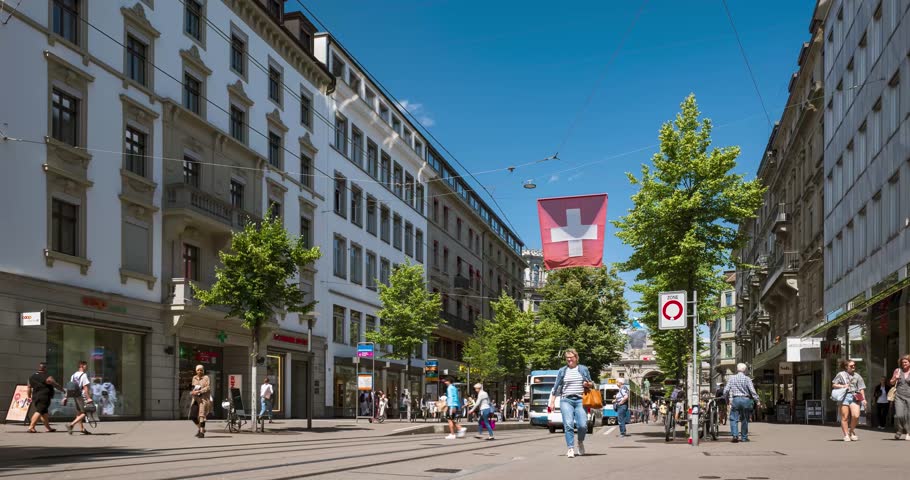 Zurich city Switzerland time lapse. Famous Bahnhofstrasse shopping street. Sunny summer day, blue sky, white clouds, tramways, pedestrians crossing, tourists walking, cars crossing the road Royalty-Free Stock Footage #1107255351