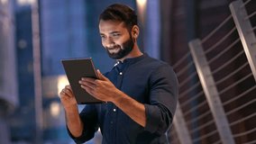 Smiling young indian business man professional, eastern businessman executive standing outdoors on street reading ebook holding using digital tablet online technology in night city with urbans lights. - Powered by Shutterstock - Get 15% off with code: PIKWIZARD15