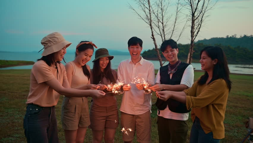 Group of young Asian people are enjoy camping , playing sparkler in natural campsite at twilight
