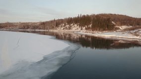 An aerial video of a frozen river with trees on the shore in winter