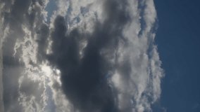 The midday sky is filled with puffy white clouds that occasionally block the sun. Sky background timelapse video. Vertical video.