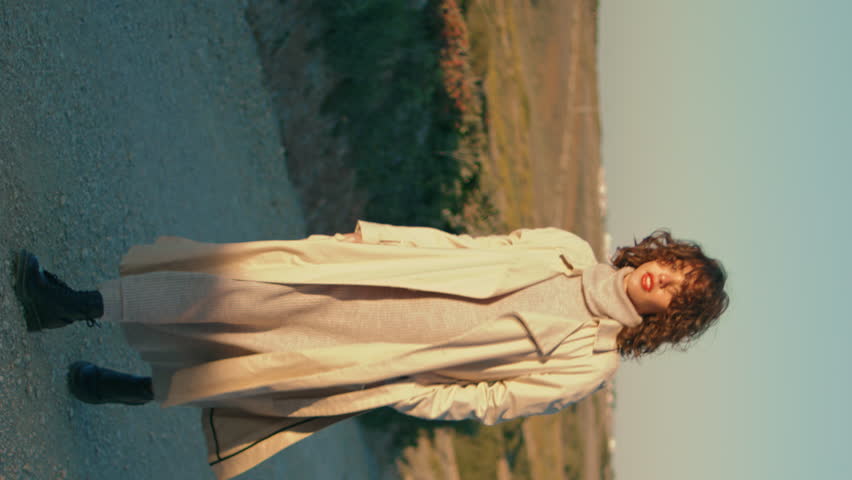 Relaxed girl walking pathway in autumn sunlight vertical. Smiling woman enjoying nature landscape going evening meadow. Serene tourist going country road resting outdoors. Relaxing weekend concept.