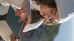 Smiling woman enjoying literature at beautiful ocean vertical. Calm sea morning. Pretty girl reading book relaxing on rocky cliff. Reader look camera in spring sunlight. Weekend leisure hobby concept - Powered by Shutterstock - Get 15% off with code: PIKWIZARD15