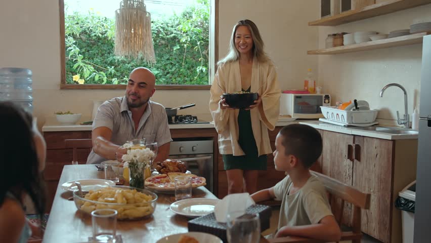 Family of Happy Man and Woman with Young Children Eating Food at Dinner Table in Home Kitchen. Parent Serving Prepared Lunch Meal or Breakfast for Kids. View on Emotional Bonding at Siblings Gathering
