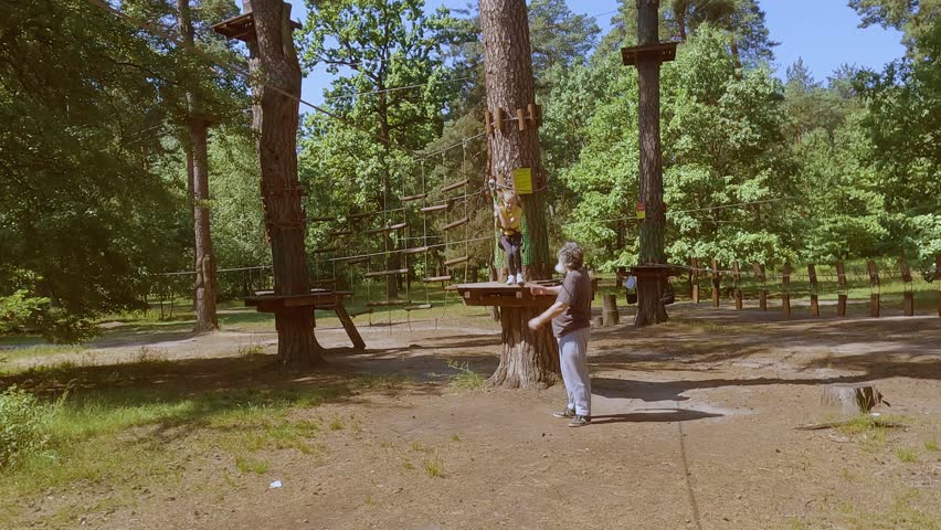 A child in a forest adventure park made of ropes. The girl is climbing the path with a high rope. Children