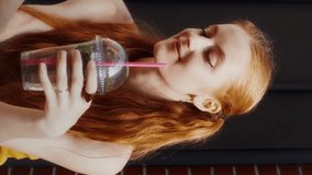 A young red-haired woman drinks a mojito and uses a mobile phone while sitting on a city street - Powered by Shutterstock - Get 15% off with code: PIKWIZARD15