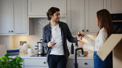 Excited couple celebrating with glass of red wine in kitchen of new home as they unpack boxes on moving in day together - shot in slow motion วิดีโอสต็อก