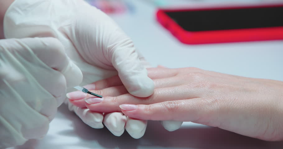 Closeup view of the elegant female hands. The manicurist covers client's nails with transparent nail polish or special protective liquid in the cosmetology studio. Beauty and cosmetology concept Royalty-Free Stock Footage #1107296379