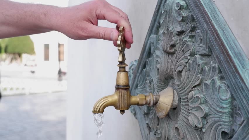 A man opens a faucet with water, the faucet of an ancient mosque in gold color, the concept of Islamic ablution, the historical mosques of Istanbul