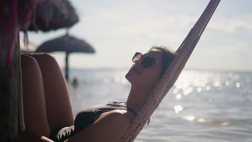 Peaceful attractive young woman relaxing in a hammock on vacation. Healthy calm girl relaxing on a comfortable outdoor swinging hammock, dream, stress-free, relaxing on vacation, dreaming of good
