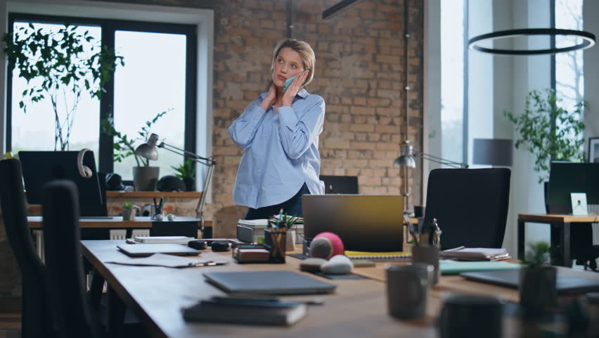 Woman calling in empty office walking near wooden conference table. Relaxed businesswoman talking smartphone at modern workplace. Confident female manager have friendly phone conversation in company. Royalty-Free Stock Footage #1107300101
