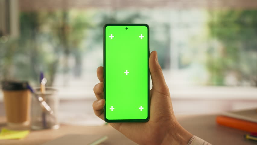 Anonymous Businessman Holding Smartphone with Green Screen Mock Up Display, Making a Video Call in a Creative Office Environment. Virtual Meetings, Modern Technology and Remote Work Concept