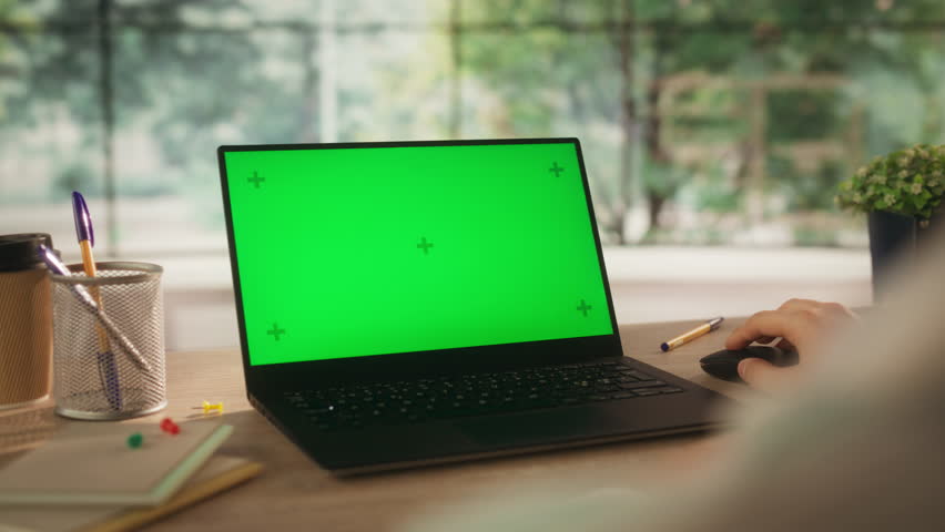 Over the Shoulder Footage with a Small Business Owner Working Remotely from Home, Using Laptop Computer with Mock Up Green Screen Display. Person Sitting Behind a Cozy Wooden Desk, Browsing Internet Royalty-Free Stock Footage #1107300687