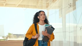 Education concept, female student. Happy lovely brazilian female student, with a backpack, hold books and notebooks in her hand, stand near the university campus, looks away and smile. Copy-space - Powered by Shutterstock - Get 15% off with code: PIKWIZARD15
