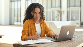 Confident successful smart curly haired girl, brazilian or hispanic nationality, freelancer worker or student, uses laptop to work or study online while sitting outdoors, takes notes in notebook,smile - Powered by Shutterstock - Get 15% off with code: PIKWIZARD15