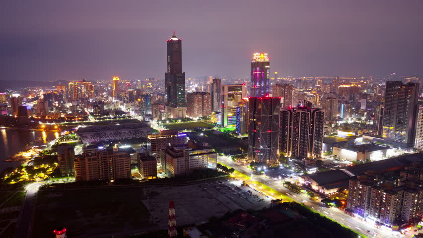 Aerial hyperlapse of Kaohsiung, a vibrant seaport city in Southern Taiwan, with 85 Sky Tower standing out in downtown next to the harbor, city lights dazzling in the night and busy traffic on streets